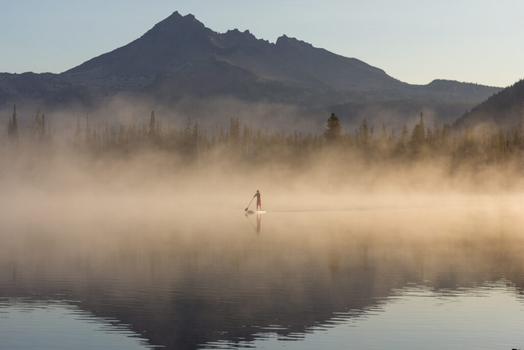 A man paddle boarding on a foggy lake.