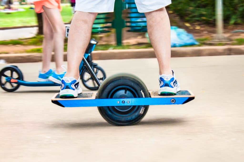 A man wearing blue running shoes and shorts riding a onewheel xr.