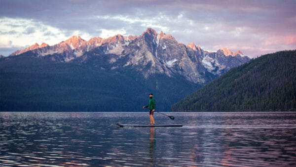 A man paddle boarding on a lake with mountains in the background.