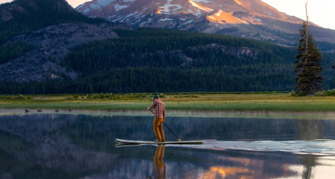 A person paddle boarding down a river with a mountain.