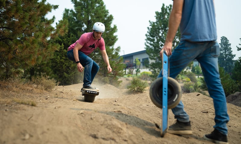 Man riding a Onewheel off-road while someone else watches.