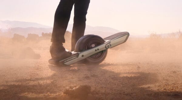 A person with a foot on one edge of the Onewheel GT in the middle of a desert.